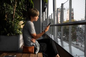 mulher asiática verificando seu smartphone ao à frende da janela